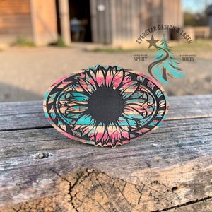 May include: Oval wooden coaster with a sunflower design. The coaster features a black center and a turquoise, pink, and tan patterned border. The text "EVERSTAR DESIGN & LASER" is visible in the upper right corner.
