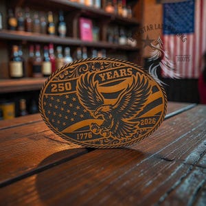 May include: An oval belt buckle featuring a laser-engraved design of a bald eagle with wings spread. The background includes stars and stripes with the text 250 YEARS, 1776, and 2026. The border has a decorative floral pattern.