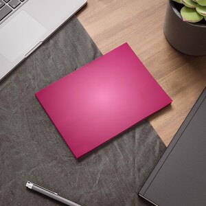 May include: A blank pink card on a gray textured surface with a laptop and a potted succulent plant in the background.