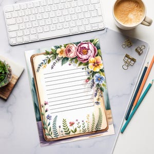 May include: A lined notepad with a floral border featuring pink, yellow, and purple flowers. The notepad is on a desk with a keyboard, coffee cup, pencils, and paper clips. The floral design includes roses, pansies, and other wildflowers.