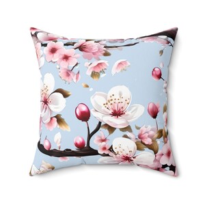 May include: A light blue cushion with a floral pattern featuring pink and white cherry blossoms on a branch. The cushion has a soft, plush feel and is perfect for adding a touch of spring to any room.