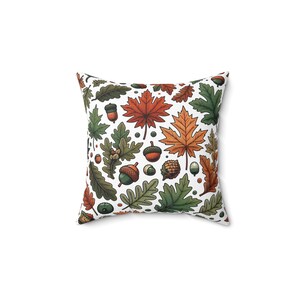 May include: A white throw pillow with a colourful autumn leaf and acorn pattern. The pillow features a variety of leaves in shades of green, orange, and red, as well as acorns in brown and tan.