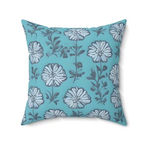May include: A turquoise blue cushion with a floral pattern. The flowers are white with a grey outline and are arranged in a repeating pattern.