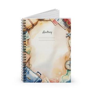 Könnte beinhalten: Spiralgebundenes Notizbuch mit Reisemotiv. Das Cover zeigt Aquarellillustrationen von Gepäck, Pässen, einem Kompass und einem kleinen Flugzeug. Der Name "Audrey" steht auf dem Cover.
