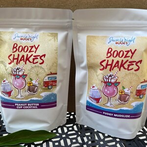 May include: Two white pouches with colorful labels. The labels say "Dream Right Boozy" and "Boozy Shakes". One pouch says "Peanut Butter Cup Cocktail" and the other says "Fudgy Mudslide".