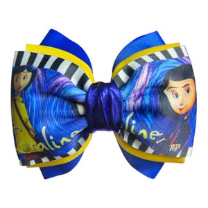 May include: A layered hair bow featuring a cartoon character design. The bow has a blue, yellow, and black and white color scheme. The word "Caroline" is printed on the bow.