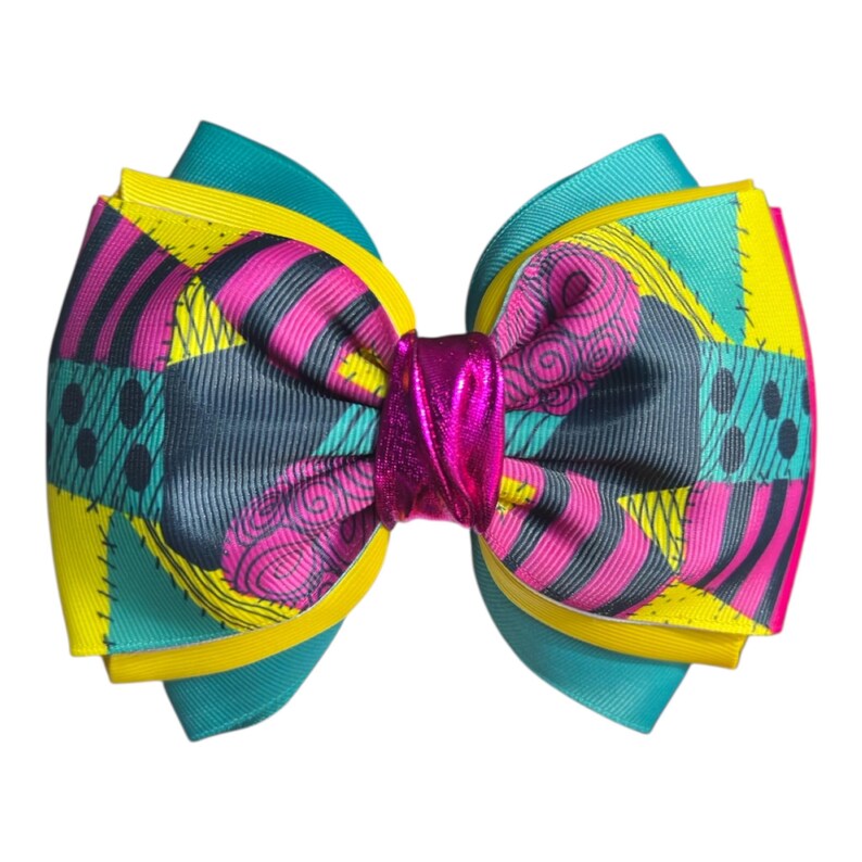 May include: A large, layered hair bow featuring a patchwork design in teal, yellow, pink, and gray. The bow has a metallic pink center and is suitable for various occasions. The bow is a vibrant accessory.