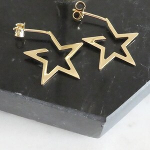 May include: A pair of gold star-shaped earrings with a simple design. The earrings are made of a thin metal and have a delicate look.
