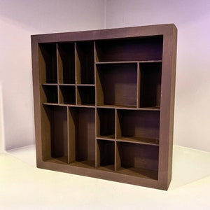 May include: A dark brown wooden shadow box with multiple compartments of varying sizes. The rectangular frame has a simple design, and the interior is divided into small, medium, and large sections. This display case is suitable for collectibles or small items.