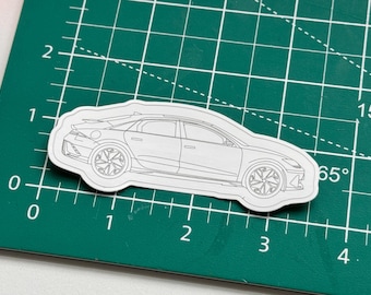 May include: A white outline drawing of a car on a green cutting mat. The car has a rounded front end and a long, sleek body.