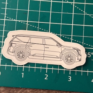 May include: A line drawing of a white SUV on a green cutting mat. The car is facing to the right and has a black outline.