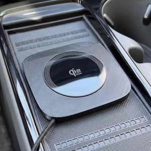 May include: A silver wireless charging pad with a black circular charging area. The charging pad is integrated into a car's console and features the text "qi2 25W". A charging cable is connected to the pad.