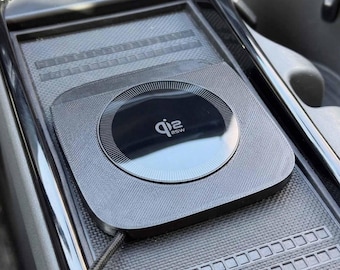 May include: A silver wireless charging pad with a black circular charging area. The charging pad is integrated into a car's console and features the text "qi2 25W". A charging cable is connected to the pad.