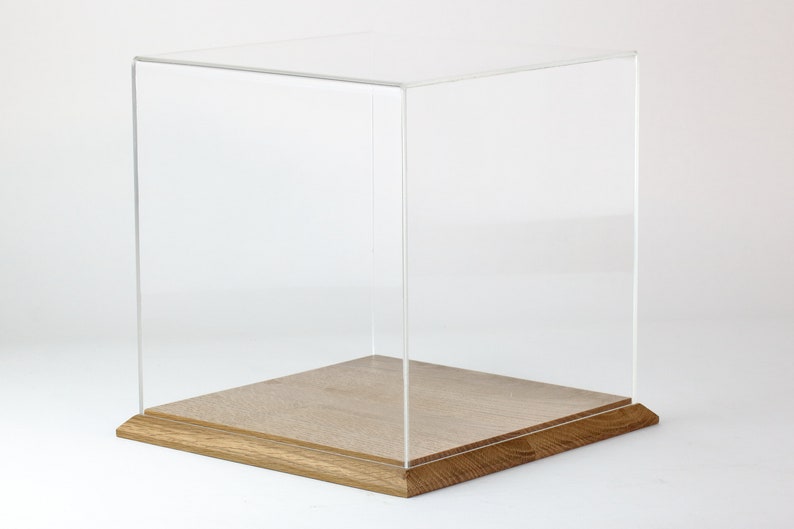 Puede incluir: Una vitrina de exhibici&oacute;n de acr&iacute;lico transparente con una base de madera. La vitrina es cuadrada y tiene una base de madera clara.