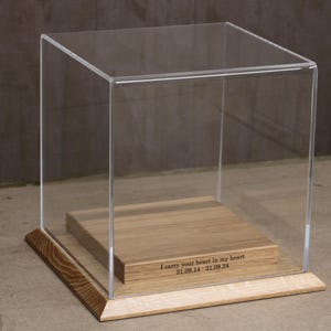 Könnte beinhalten: Eine transparente Acrylglas-Vitrine mit einem Holzsockel. Der Sockel ist mit der Botschaft "Ich trage dein Herz in meinem Herzen 31.05.14 - 31.08.24" graviert.
