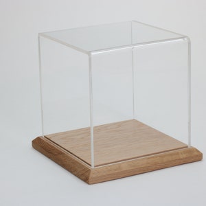 Puede incluir: Una vitrina de exhibici&oacute;n de acr&iacute;lico transparente con una base de madera. La vitrina es cuadrada y tiene un dise&ntilde;o simple.