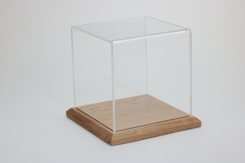 Puede incluir: Una vitrina de exhibici&oacute;n de acr&iacute;lico transparente con una base de madera. La vitrina es cuadrada y tiene un dise&ntilde;o simple.