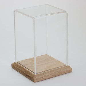 Puede incluir: Una vitrina de exhibici&oacute;n de acr&iacute;lico transparente con una base de madera. La vitrina es cuadrada y tiene un dise&ntilde;o simple.
