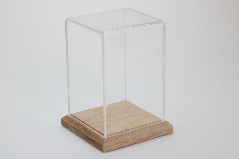 Puede incluir: Una vitrina de exhibici&oacute;n de acr&iacute;lico transparente con una base de madera. La vitrina es cuadrada y tiene un dise&ntilde;o simple.