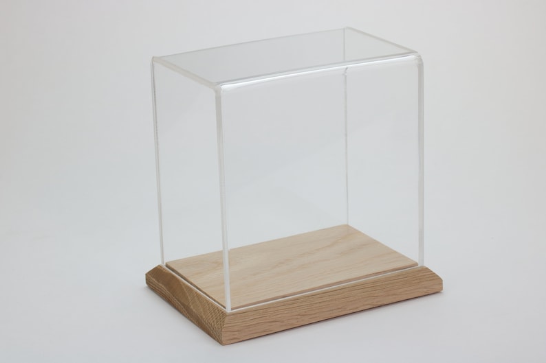 Puede incluir: Una vitrina de exhibici&oacute;n de acr&iacute;lico transparente con una base de madera. La vitrina es rectangular y tiene un dise&ntilde;o simple.