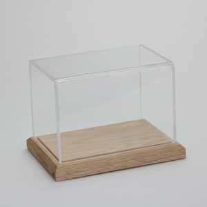 Puede incluir: Una vitrina de exhibici&oacute;n de acr&iacute;lico transparente con una base de madera. La vitrina es rectangular y tiene un dise&ntilde;o simple.