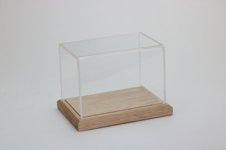 Puede incluir: Una vitrina de exhibici&oacute;n de acr&iacute;lico transparente con una base de madera. La vitrina es rectangular y tiene un dise&ntilde;o simple.