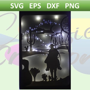 May include: A black silhouette of a cowboy riding a horse in a desert landscape with cacti, a dreamcatcher, and stars. The scene is illuminated with white lights.