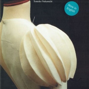 Pode incluir: Capa do livro "PATTERN MAGIC 2" de Tomoko Nakamichi, com um manequim creme com um design de tecido. A capa tem um círculo turquesa com o texto "Now in English". O pescoço do manequim é aparado em vermelho.