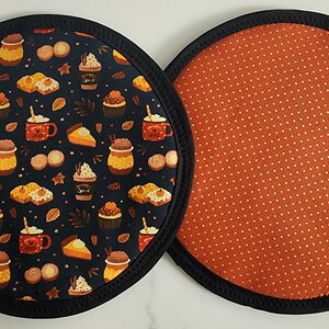 May include: Two round fabric coasters. One features a dark blue background with a pattern of fall-themed images like coffee cups, cupcakes, and pie slices. The other coaster has an orange background with white polka dots.