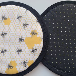 May include: Two round pot holders with black trim. One features a yellow and white honeycomb pattern with black bee illustrations. The other has a black background with white and green polka dots.
