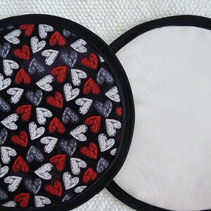 May include: Two round coasters. One coaster features a black background with a pattern of red, white, and gray hearts. The other coaster is white. Both coasters have a black border.
