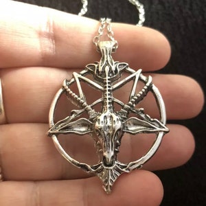 May include: Silver pendant necklace featuring a goat skull with horns inside a pentagram. The pendant is on a silver chain.