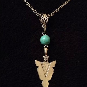 May include: A silver chain necklace with a turquoise bead and a silver arrowhead pendant.