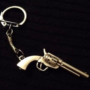Könnte beinhalten: Ein silberfarbener Revolver-Schlüsselanhänger mit einem geteilten Ring und einer Kette.