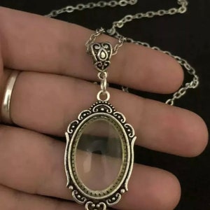 Puede incluir: Un collar de cadena de plata con un colgante que presenta un óvalo de vidrio transparente enmarcado por un diseño de plata adornado.