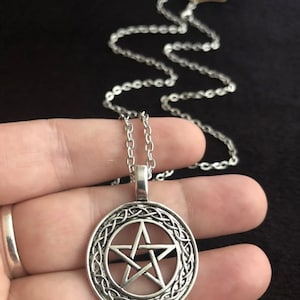 Può includere: Una collana con catena d'argento con un ciondolo circolare che presenta un pentagramma all'interno di un design a nodo celtico.