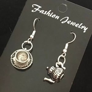 May include: A pair of silver earrings with a teacup and teapot design. The earrings are on a black card with the text "Fashion Jewelry".