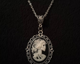 May include: A silver chain necklace with a cameo pendant featuring a white skeletal figure of a woman with a black background.