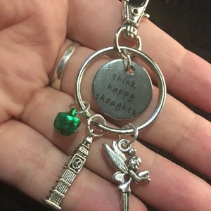 May include: Silver keychain with a charm that says "think happy thoughts" and other charms including a green bell, a silver Big Ben, and a silver fairy.