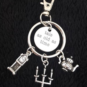 May include: A silver keychain with a charm that says "a tale as old as time". The keychain also has charms of a clock, a candlestick, and a teapot.