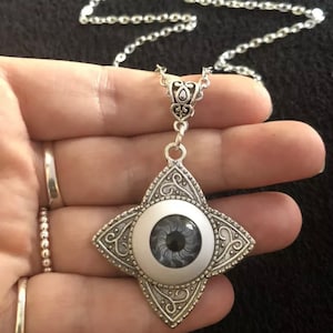 May include: A silver necklace with a star-shaped pendant featuring a black and grey eye design.