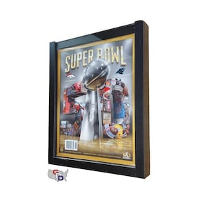 May include: A black framed picture of a Super Bowl magazine cover featuring a silver trophy with a football on top. The magazine cover has a gold background with the text "SUPER BOWL" in large white letters.