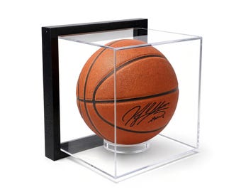 May include: A textured orange basketball with black seams and a black signature on the surface, enclosed within a clear acrylic display cube featuring a black frame and a circular clear stand to hold the ball in place.