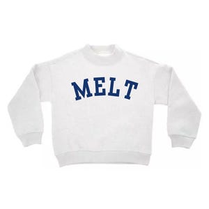 May include: A white long-sleeve sweatshirt featuring a mock neck collar and ribbed cuffs. The word MELT is printed in a bold, dark blue, arched font across the center of the chest. The garment has a relaxed fit with dropped shoulder seams.