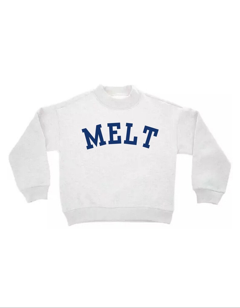May include: A white long-sleeve sweatshirt featuring a mock neck collar and ribbed cuffs. The word MELT is printed in a bold, dark blue, arched font across the center of the chest. The garment has a relaxed fit with dropped shoulder seams.