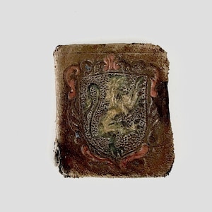 May include: A small, brown leather wallet with a detailed, embossed design of a green and gold face with a crown. The face is surrounded by pink and red floral accents.