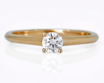 May include: A gold solitaire engagement ring with a round-cut diamond. The ring features a simple, polished band and four-prong setting, showcasing the brilliant-cut diamond. The ring is set against a white background.