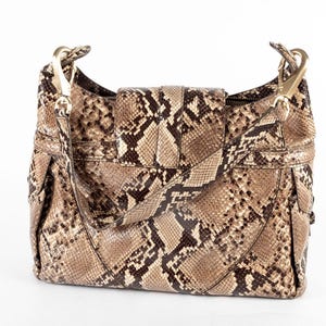 May include: A brown and tan snakeskin-patterned handbag with gold-colored hardware. The shoulder bag has a flap closure and a detachable strap. The bag is made of a textured material and has a structured shape.