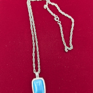 May include: A silver-toned rope chain necklace featuring a rectangular pendant with a smooth, light blue cabochon stone set in a polished silver-colored frame. The necklace includes a small circular spring ring clasp for secure closure.