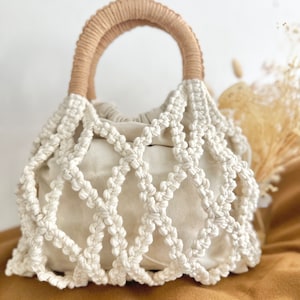 Puede incluir: Un bolso blanco de crochet con un asa de madera marrón. El bolso tiene un diseño tejido y es perfecto para llevar objetos pequeños.